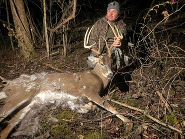 Hunter posing with large buck deer at night in the forest.