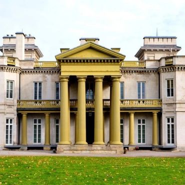 Grand neoclassical building with yellow columns and a green lawn.