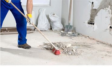Worker sweeping construction debris on a dusty floor.