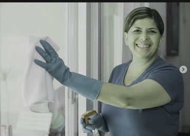 Woman wearing gloves cleaning a glass door with a cloth.