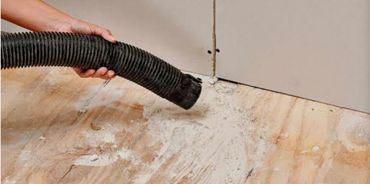 Vacuuming dust and debris from a wooden floor near a wall corner.