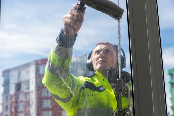 Worker cleaning a high-rise window wearing safety gear and headphones.