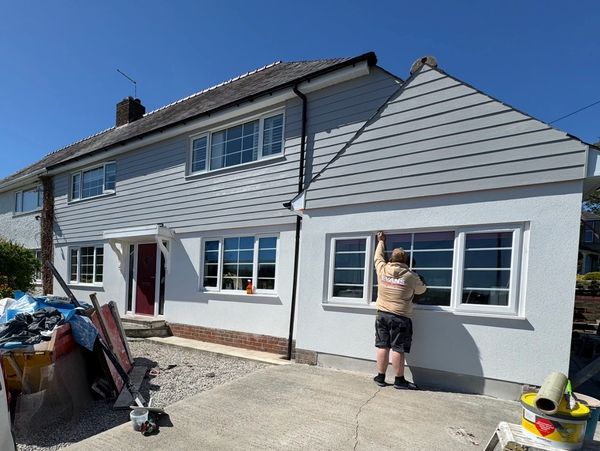 A person working on the exterior of a white and gray house on a sunny day.