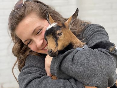 A woman warmly hugging a small brown and black goat.