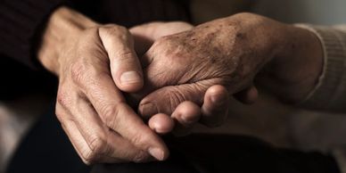 The hands of one person gently cupping the hand of a more elderly person.