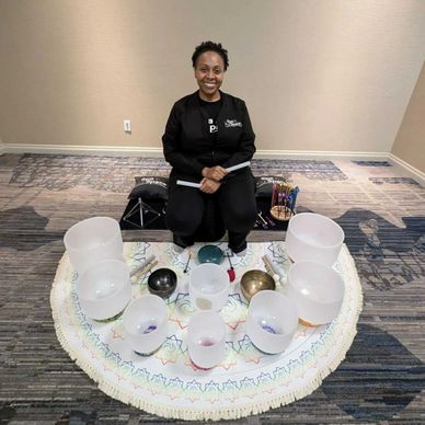 A woman sitting on the floor surrounded by crystal singing bowls and sound healing tools.