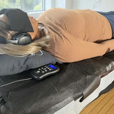 Woman lying down with headphones and eye mask, relaxing on a bed.