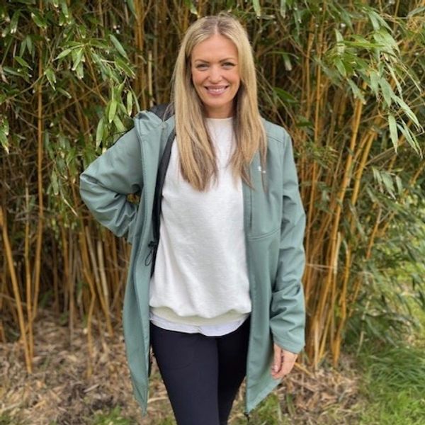 Smiling woman in casual jacket standing outdoors by bamboo plants.