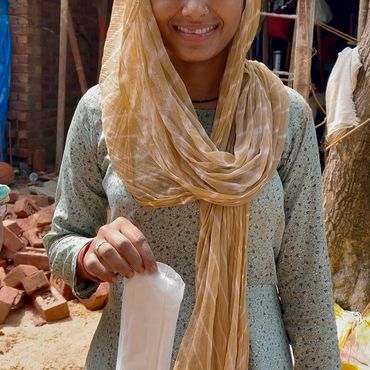 Smiling woman in traditional attire holding a sanitary pad outdoors.