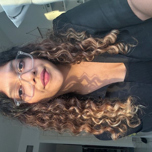Woman with curly hair and glasses in soft natural light.