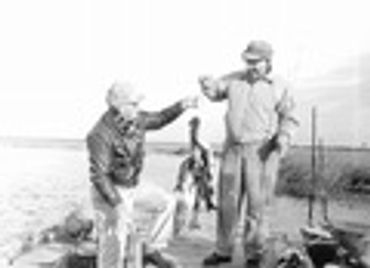 A man helps a young boy try on a fishing hat outdoors.