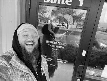 A man with a beard and yellow beanie takes a selfie outside a creative studio.