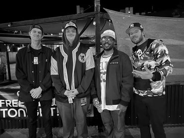 Four men posing together outdoors at night, dressed casually.