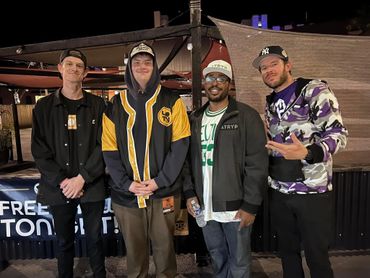 Four men posing together outdoors at night, dressed casually.