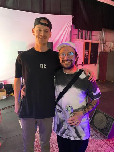 Two smiling men posing together in a casual indoor setting with colorful lighting.