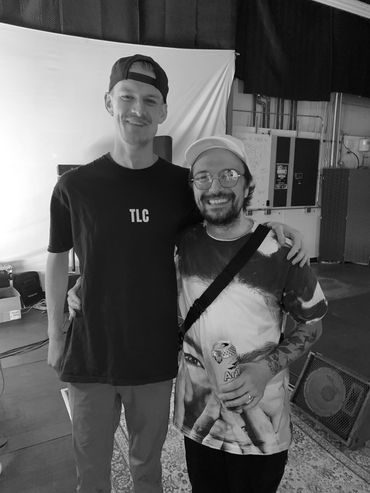 Two smiling men posing together in a casual indoor setting with colorful lighting.