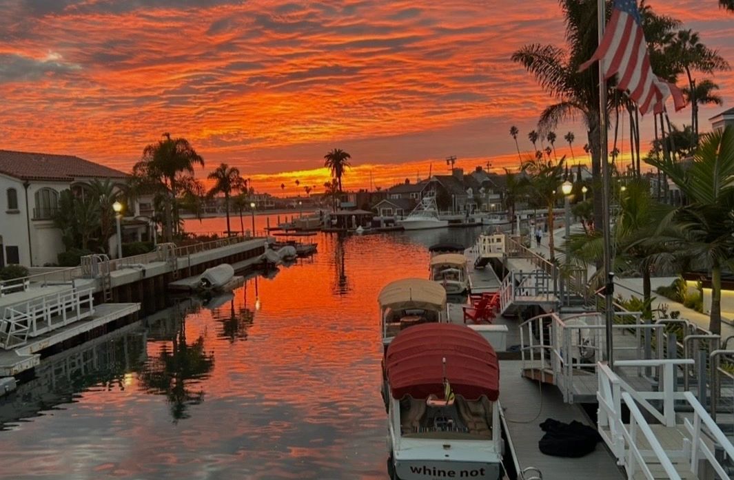 Vibrant orange sunset over a peaceful canal with boats and palm trees.