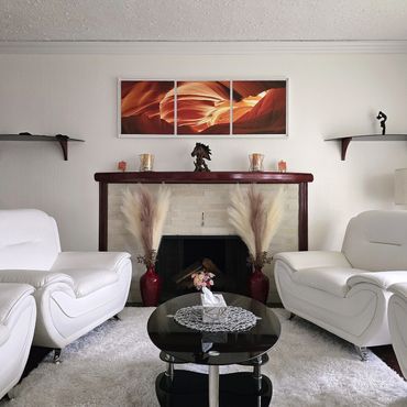 Elegant living room with white sofas, a black coffee table, and a triptych art piece above the fireplace.