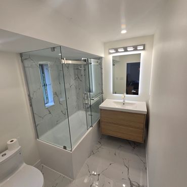 Modern bathroom with marble flooring, glass shower enclosure, and wooden vanity.