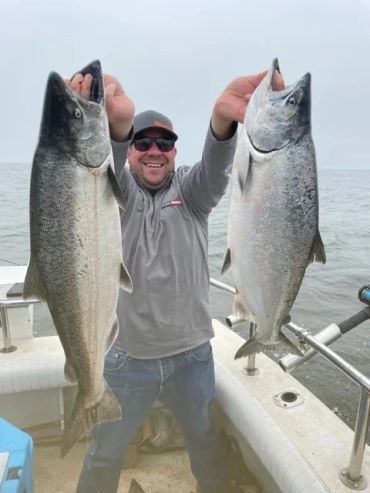 Man holding two large fish on a boat.