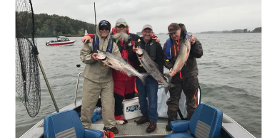 Group of four people holding fish on a boat.
