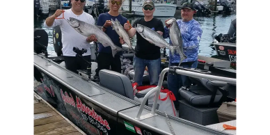 Four men on a boat holding large fish.