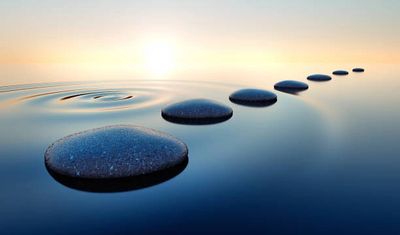 Smooth stones form a path across calm water at sunrise.