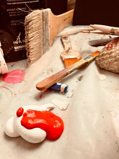 Paintbrushes and paint blobs on a messy artist's workspace.