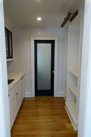 Modern pantry with white cabinetry, wood flooring, and a frosted glass door.