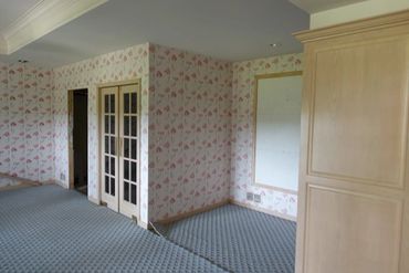 Empty room with floral wallpaper, blue carpet, and wooden doors.