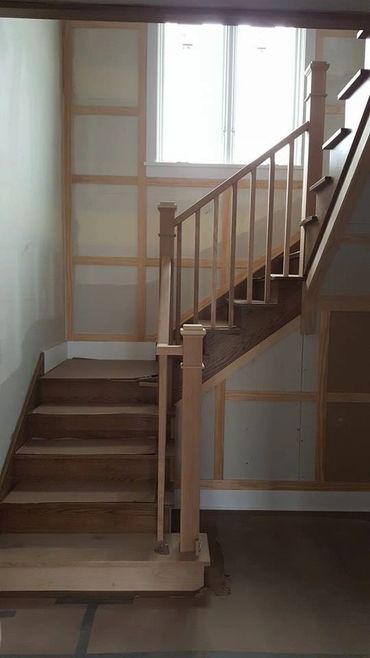 Wooden staircase with a railing in a room under construction.