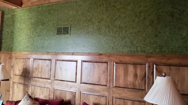 Wood-paneled wall with green textured wallpaper and a lamp in a cozy room.
