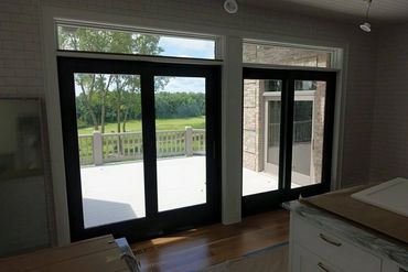 Black-framed glass doors open to a bright deck and green landscape outside.