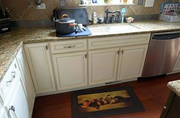 Cozy kitchen corner with granite countertops, white cabinets, and a fruit-themed floor mat.