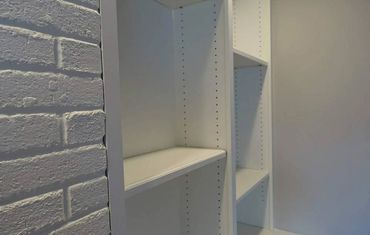 Empty white shelving unit next to a white brick wall.