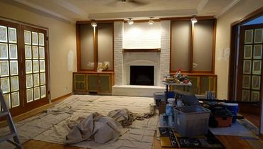Living room under renovation with paint supplies and drop cloths covering the floor.