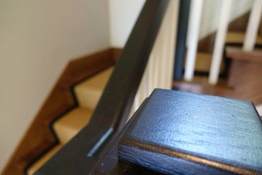 Close-up of a polished wooden stair railing with blurred stairs in the background.