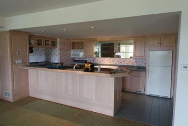 Vintage kitchen with light wood cabinetry and floral wallpaper, featuring a breakfast bar and appliances.