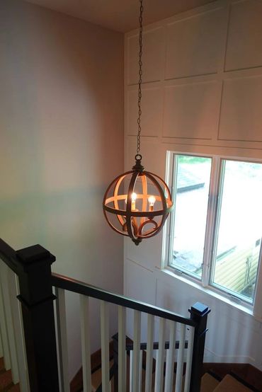 Modern spherical chandelier hanging in a stairwell with white walls and a window.