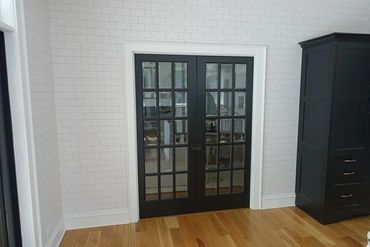 Black framed glass double doors against white tiled wall and wooden floor.