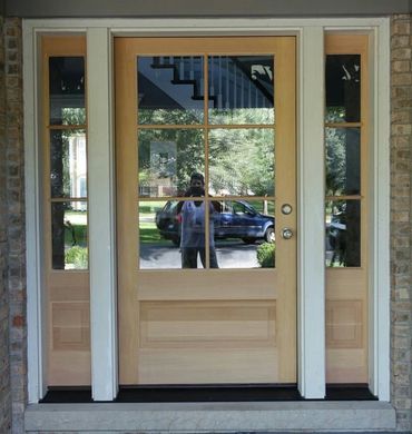 Reflection of a person taking a photo on a glass-paneled wooden front door.