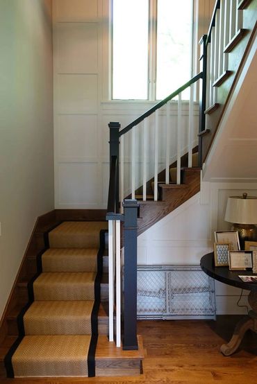 Wooden staircase with beige carpet runner and black trim in a bright hallway.