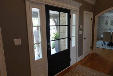 Interior view of a home entrance with a black front door and a glimpse of a dining room.
