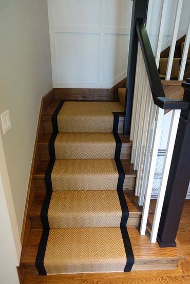 Wooden staircase with a beige carpet runner bordered in black.
