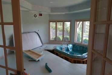 Indoor hot tub area under renovation with scattered materials and large windows.