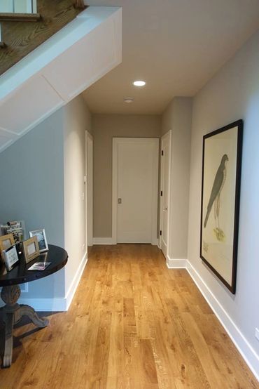 Hallway with wooden floor, white doors, bird artwork, and a table with picture frames.