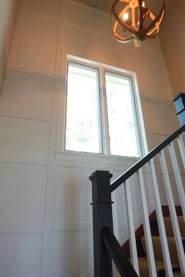Bright stairwell with white paneled walls and a modern chandelier.