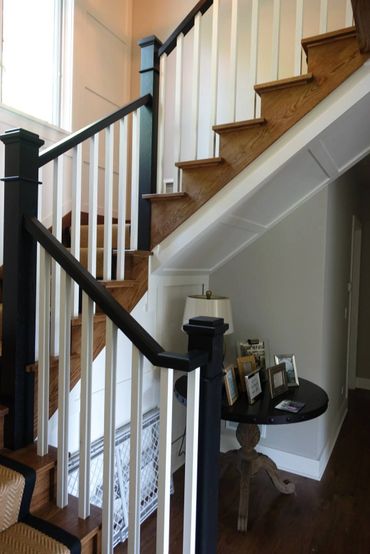Wooden staircase with black and white railing next to a round table with picture frames and lamp.