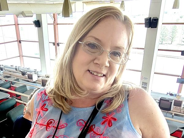 Smiling woman in a blue and pink embroidered top indoors.