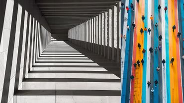 Colores Urbanos” es una obra vibrante que combina elementos de la vida urbana con un retrato moderno. El lado izquierdo muestra personas caminando frente a un muro de colores cálidos y fríos, mientras el lado derecho presenta un rostro estilizado con líneas y tonos brillantes.